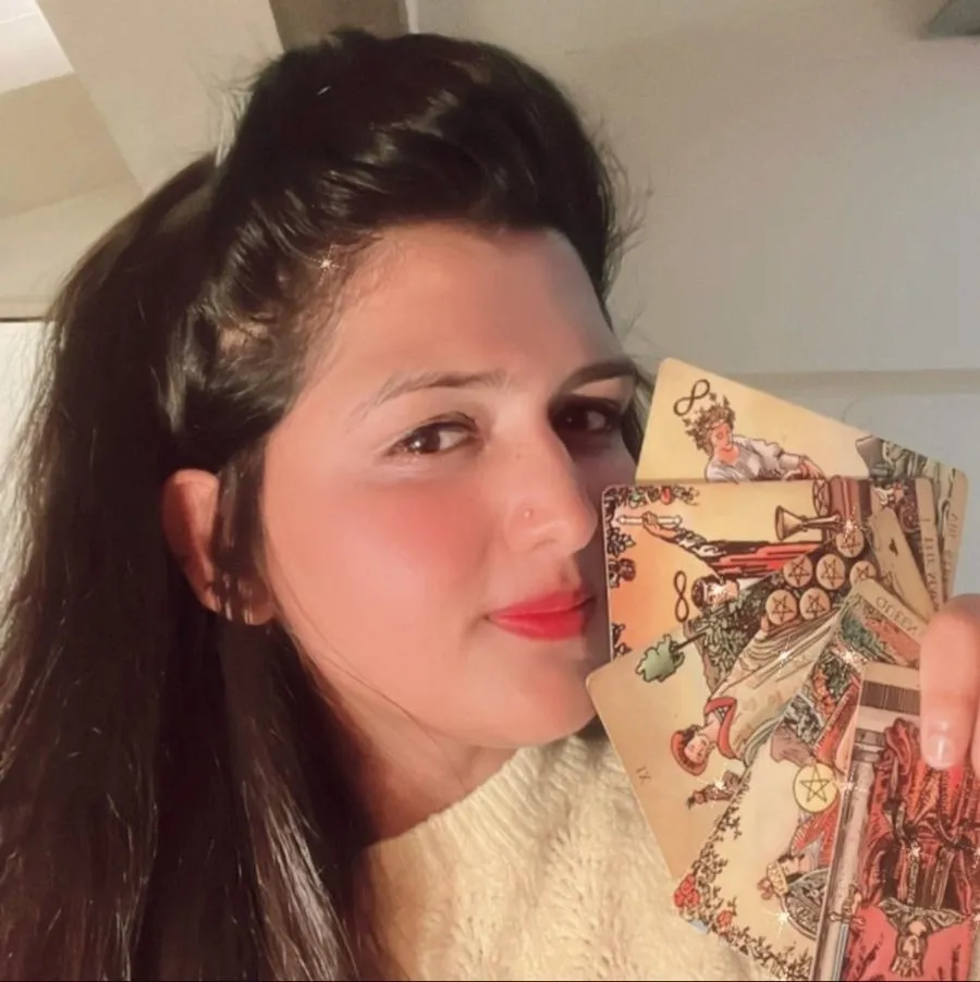 Ami Shah smiling, holding a fan of tarot cards beside her face